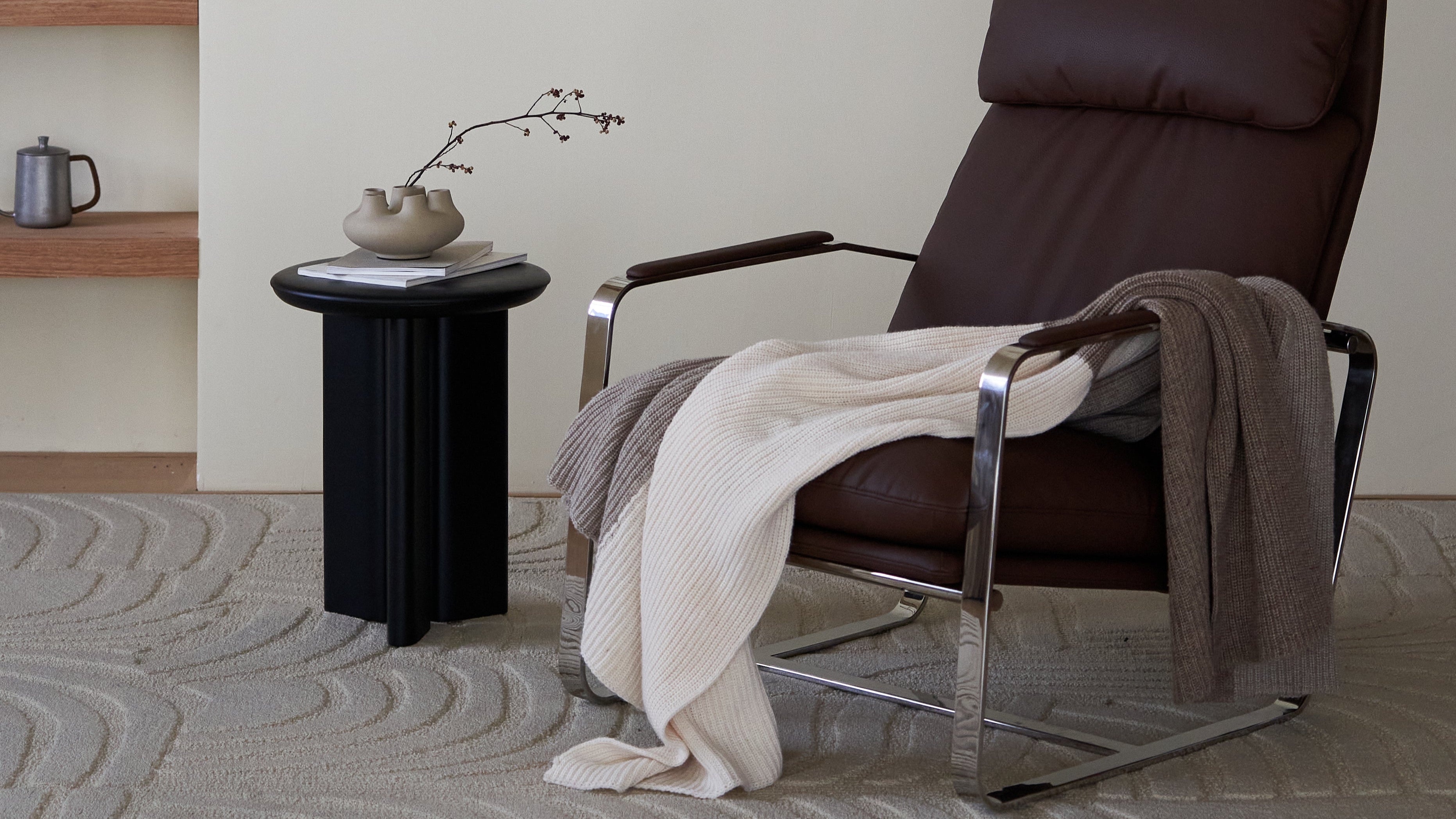 Brown recliner chair with a blanket in a room with a shelf and framed picture on the wall.