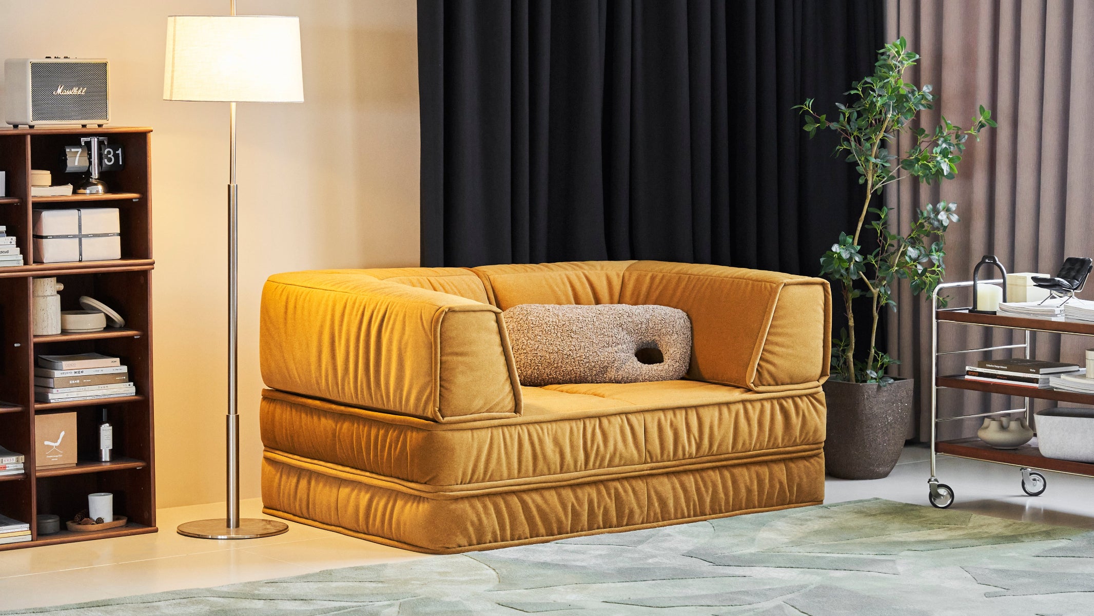 Yellow sofa in a living room setting with a lamp, bookshelf, and plant.