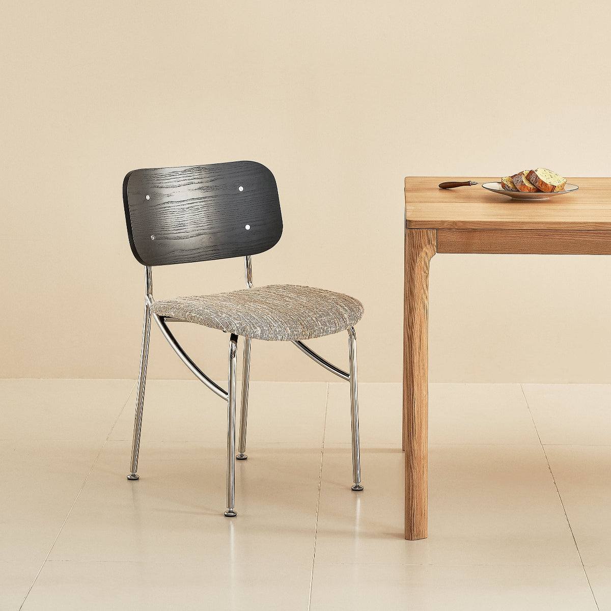 Chair next to a wooden table with a plate of food against a beige wall with a framed picture.