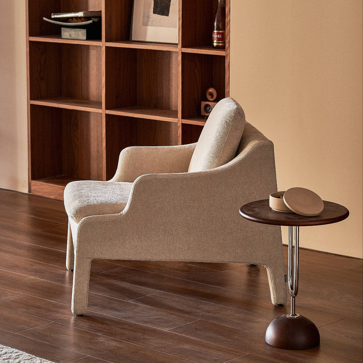 Beige armchair in a room with wooden shelves and a small round table.