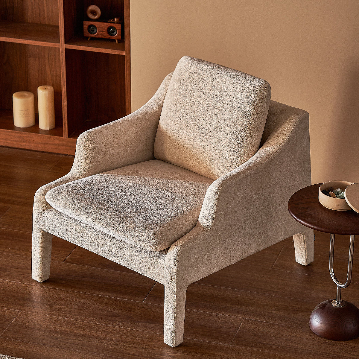 Beige armchair in a room with wooden floor and bookshelf.