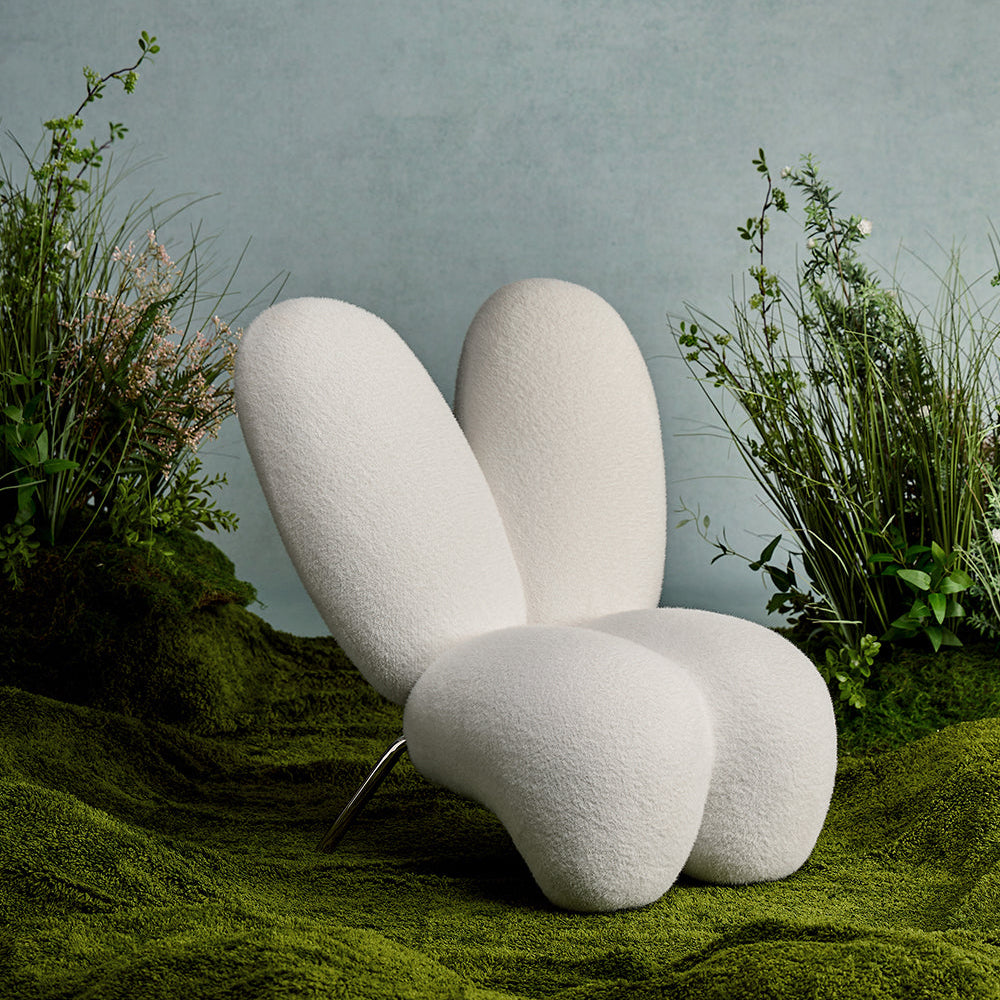 Modern white chair in a natural setting with plants and a textured wall.