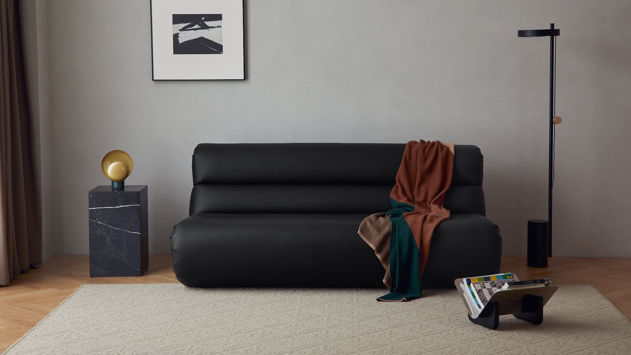 Modern living room with a black sofa, marble side table, and abstract art on the wall.