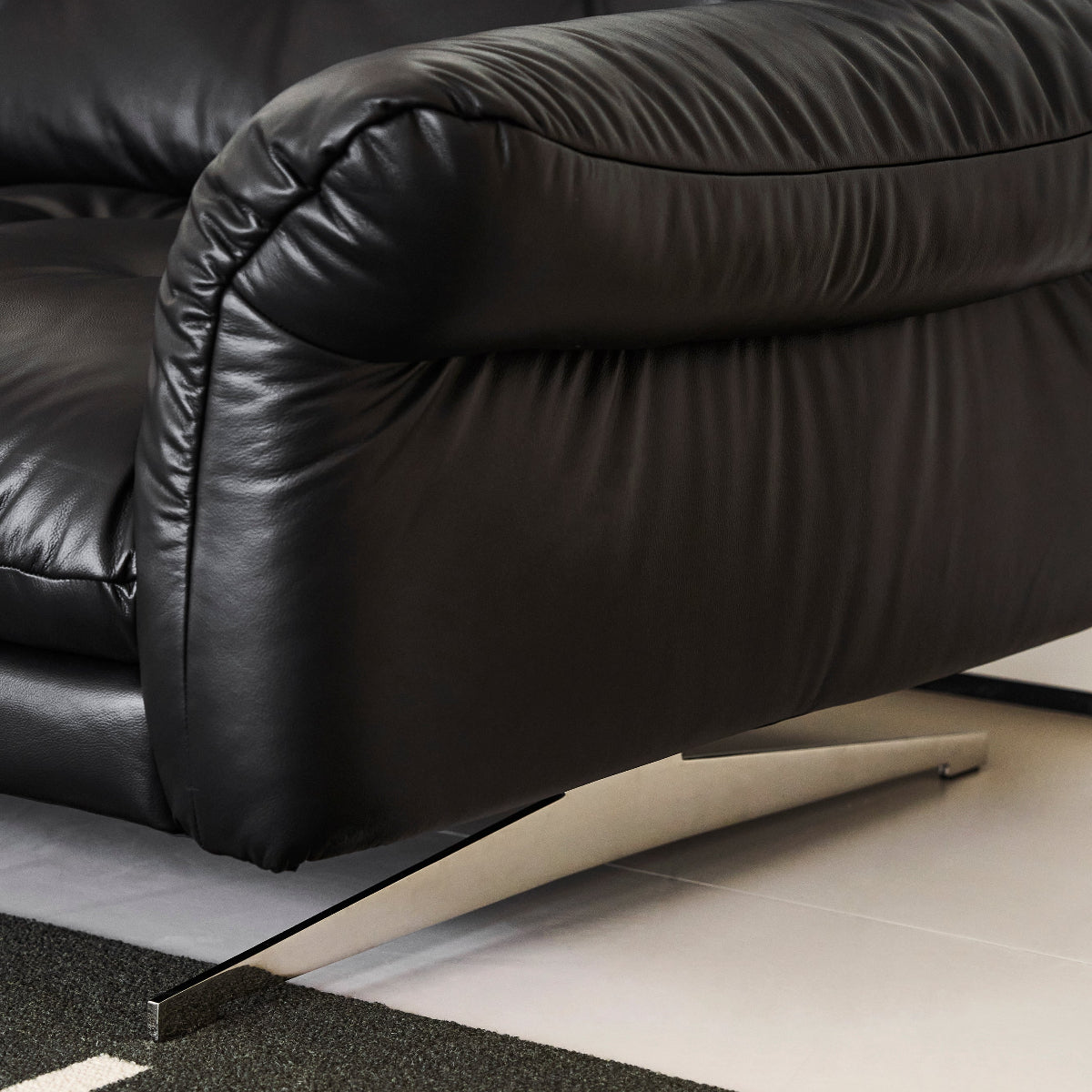 Close-up of a black leather sofa with a geometric patterned rug underneath.