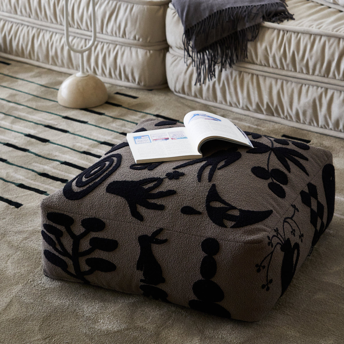 Patterned ottoman with a book on a rug in front of a beige sofa.