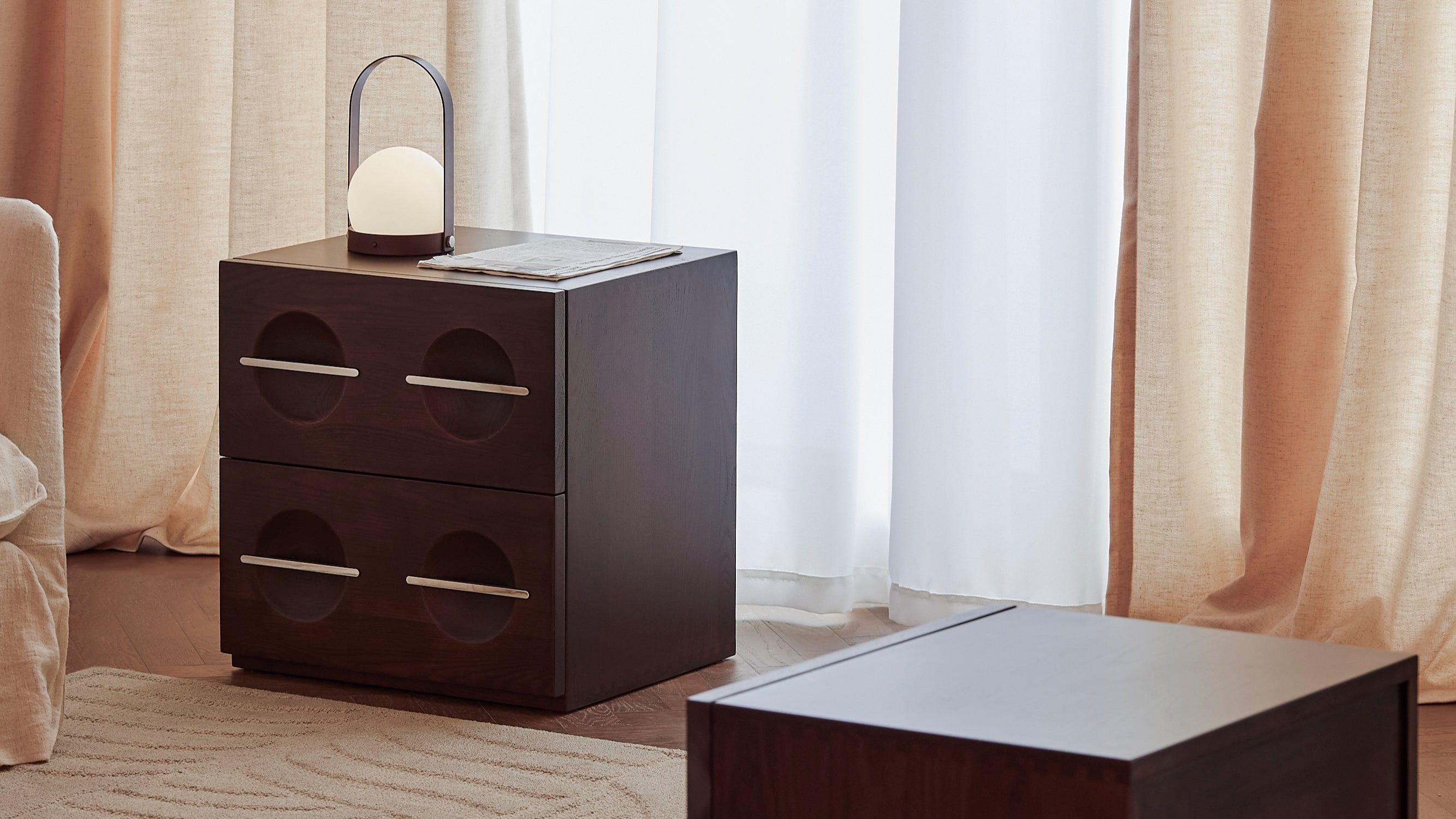 Dark wooden side table with a lamp against a neutral curtain backdrop